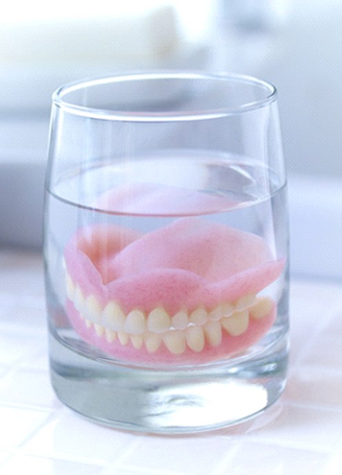 Dentures in Norton Shores soaking in glass on bathroom counter
